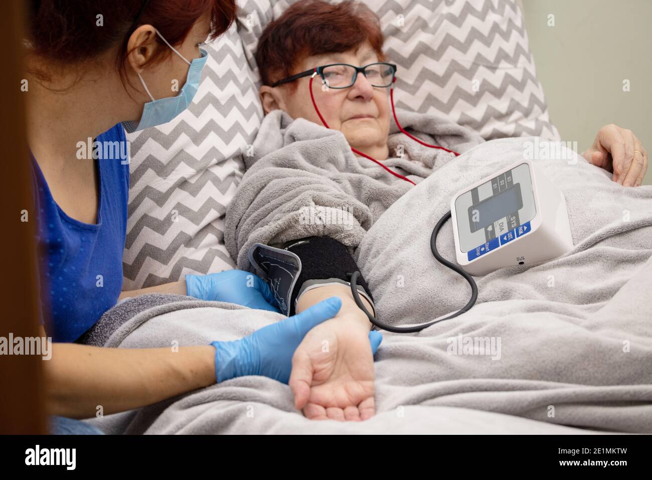 Sick senior woman lies in a bed and reads a book , Senior woman reading book with nurse Stock Photo