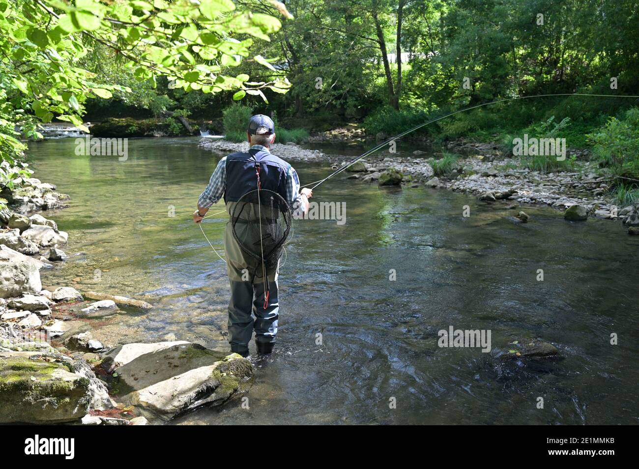 fly fisherman in summer fishing in a mountain river with waders and a cap Stock Photo