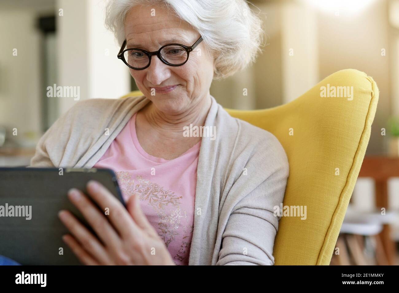 Senior woman relaxing in armchair and using digital tablet Stock Photo