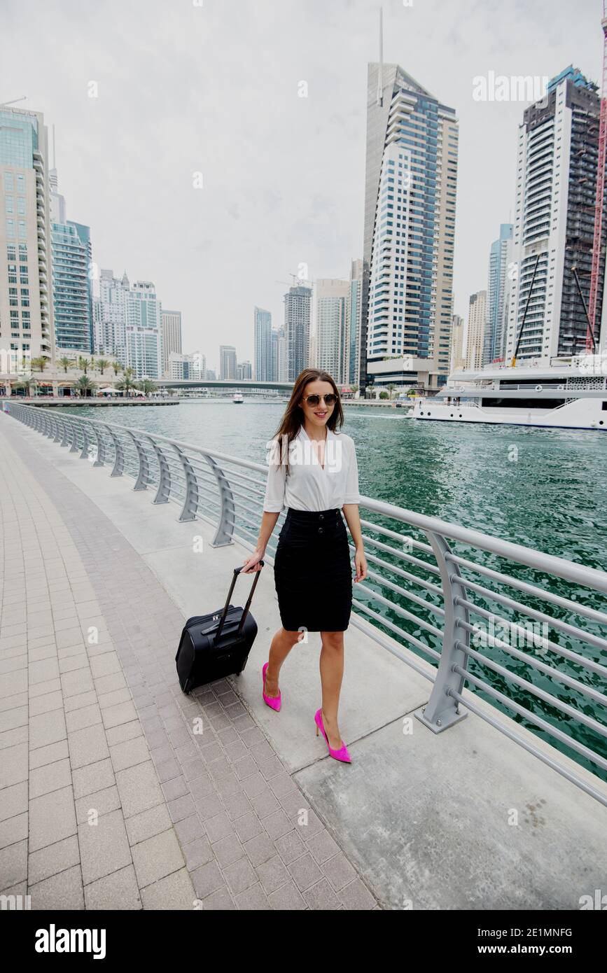 Busy young modern business woman in suit pulling a suitcase in a Dubai ...