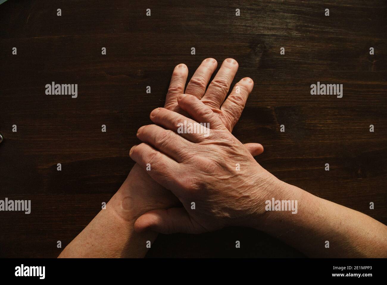 Hands and arms of old man lying on top of wooden table surface. Directly above. Stock Photo