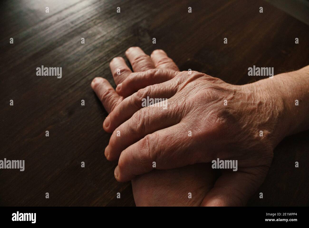 Hands of old man on wooden table. Hand over hand. High angle view. Stock Photo