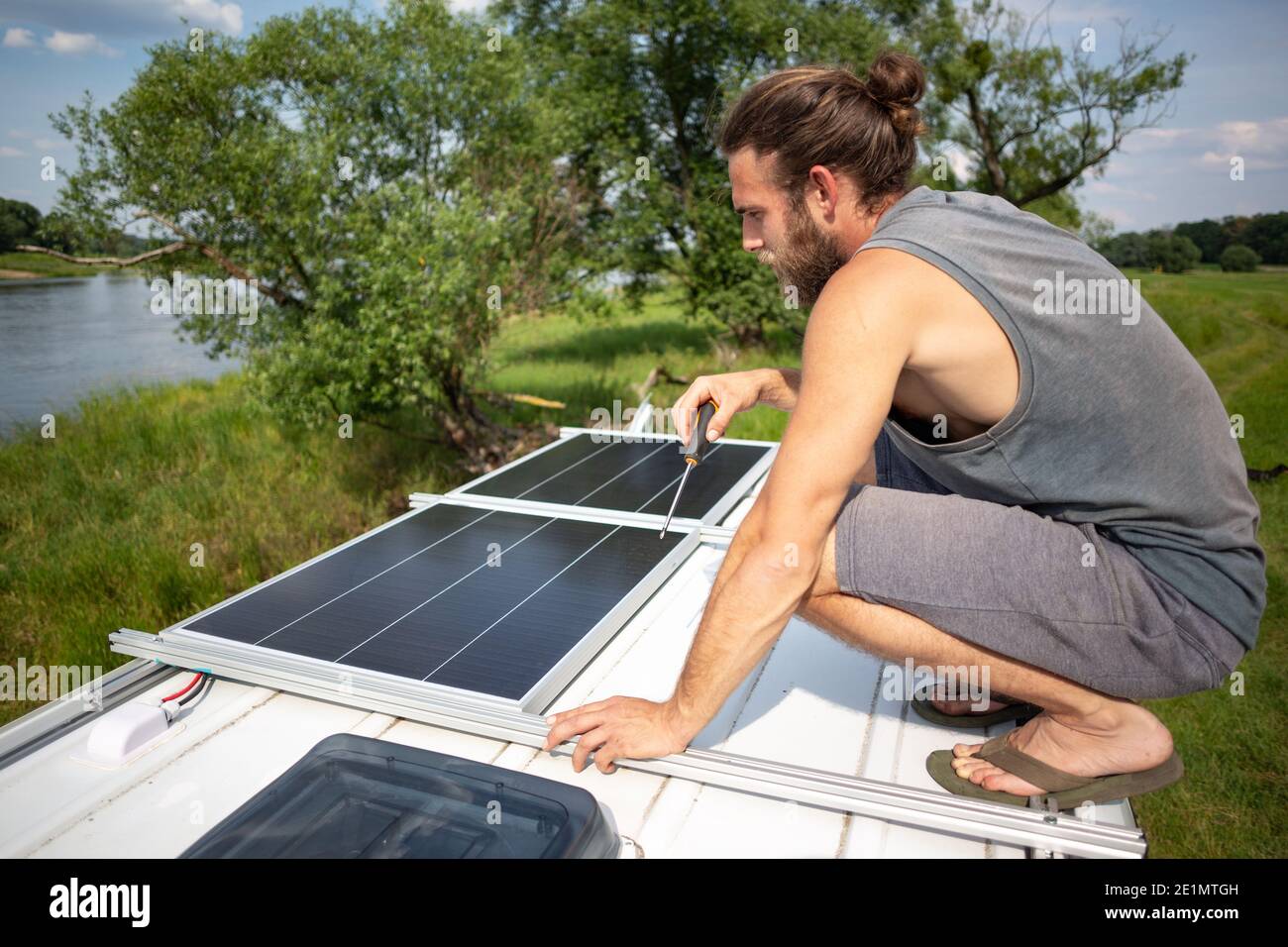Man on top of a camper van next to solar panels Stock Photo