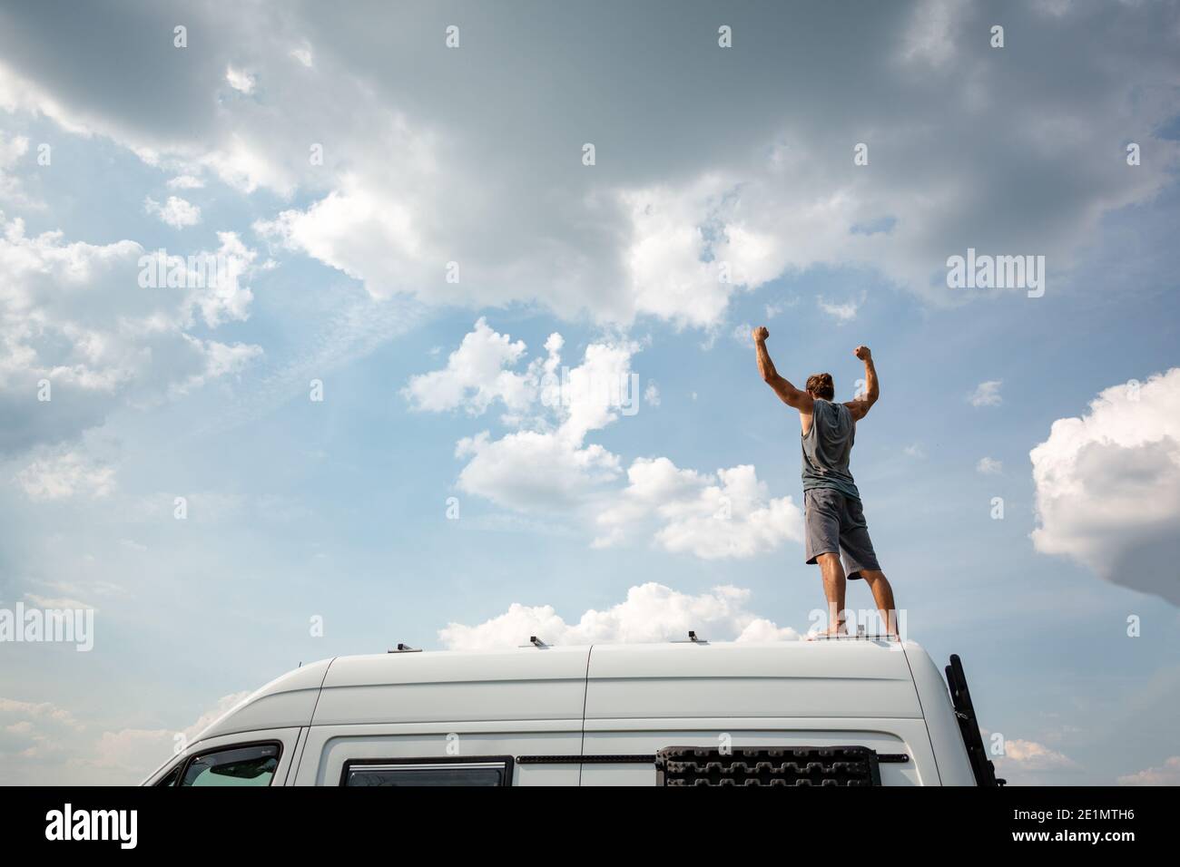 Man with raised arms standing on top of his camper van Stock Photo