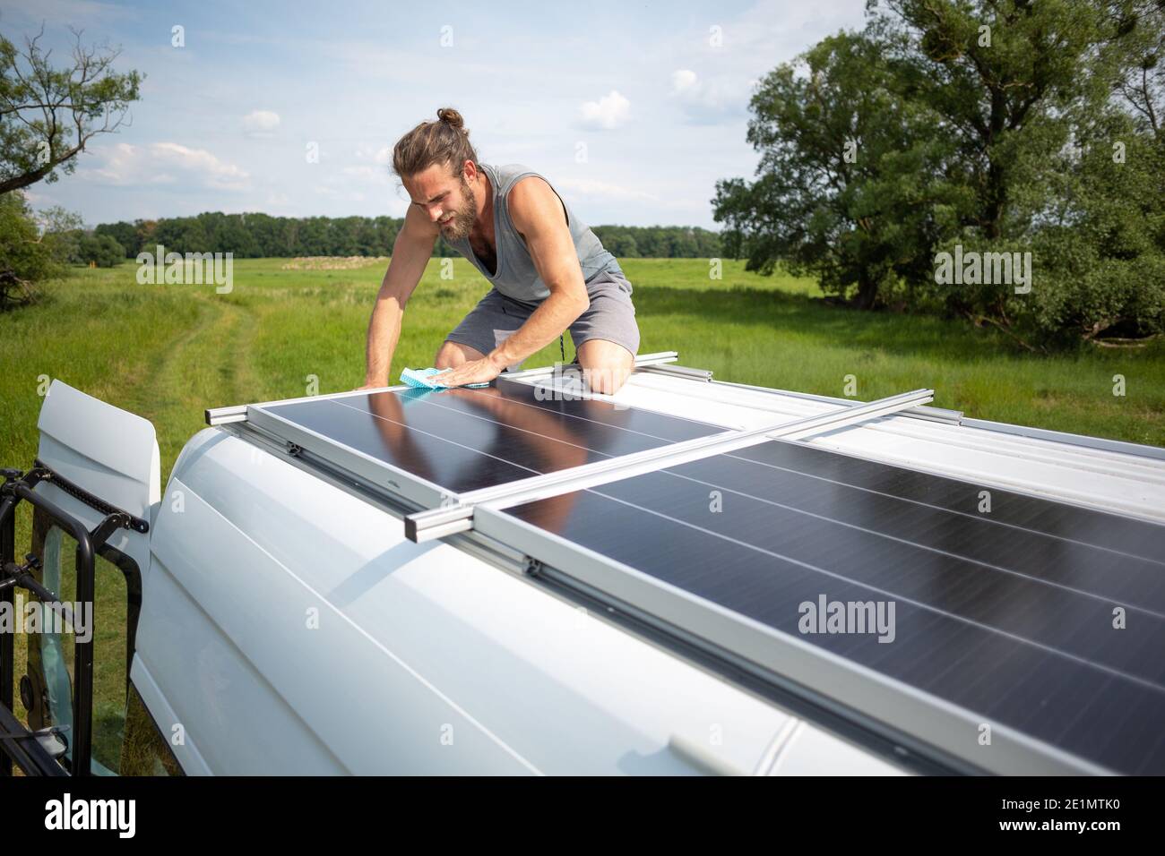 Man wiping a solar panel on top of a camper van Stock Photo