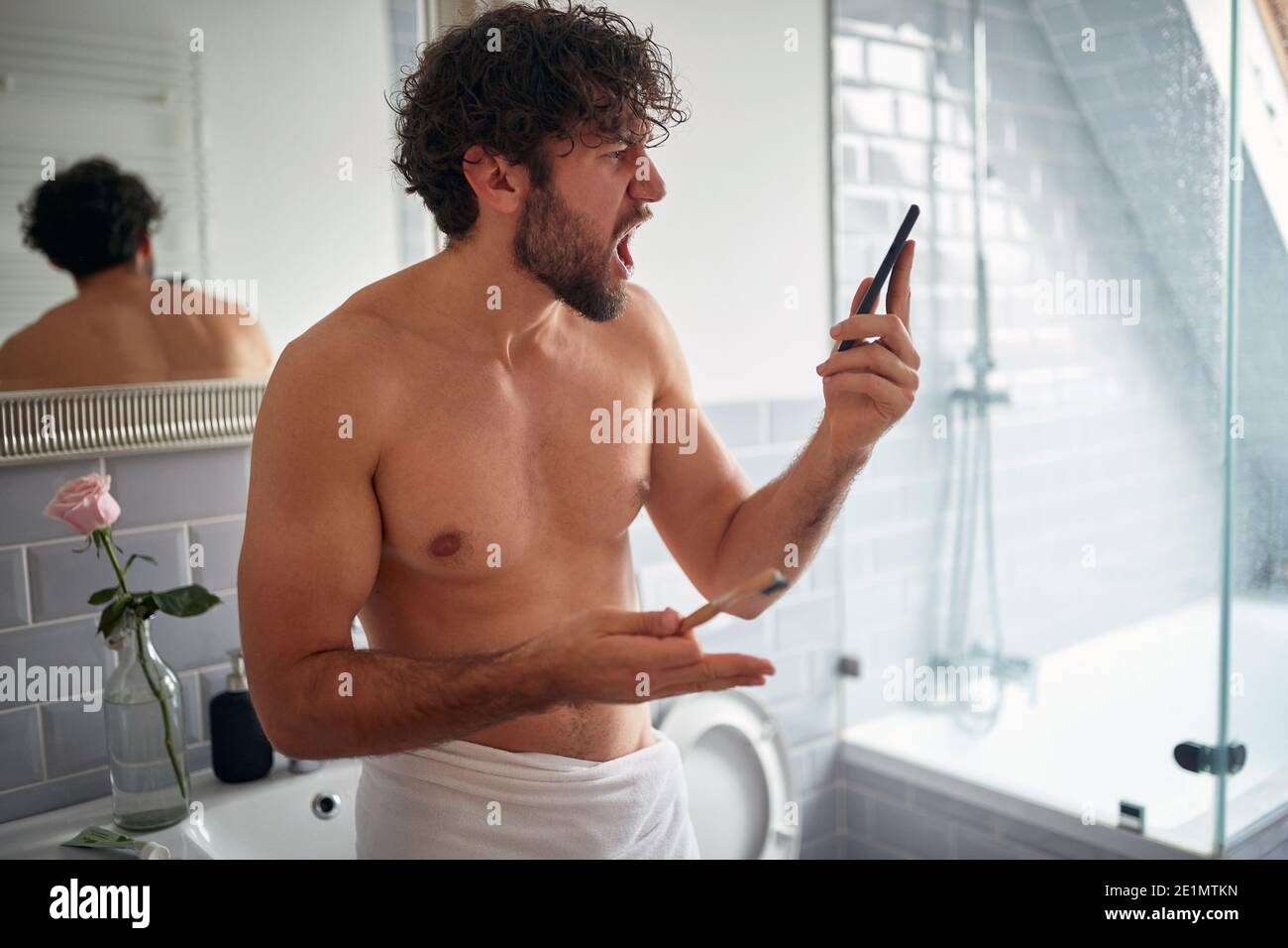 Young handsome man angry about a call while brushing teeth in a relaxed atmosphere of the bathroom. Hygiene, bathroom, morning Stock Photo