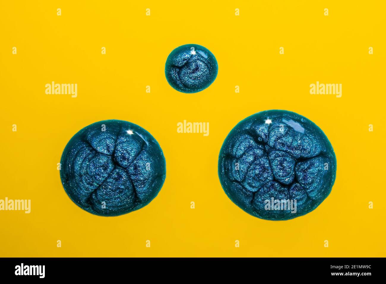 Blue sparkly paint drops on yellow background Stock Photo