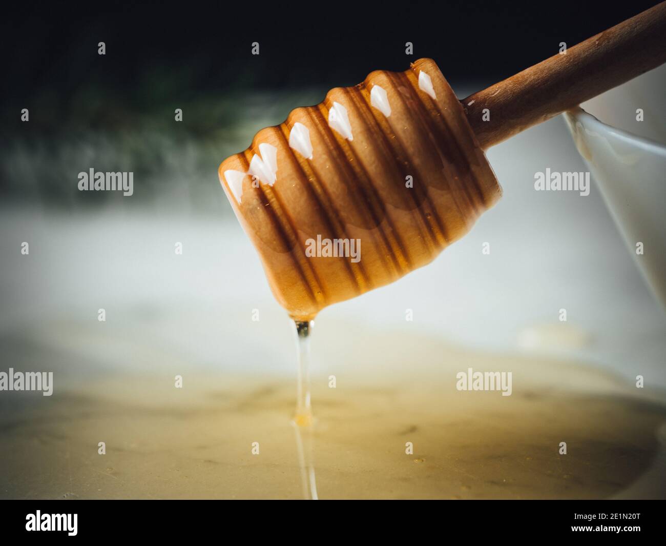 Honey wood dipper is pouring honey. Honey dripping on white marble top