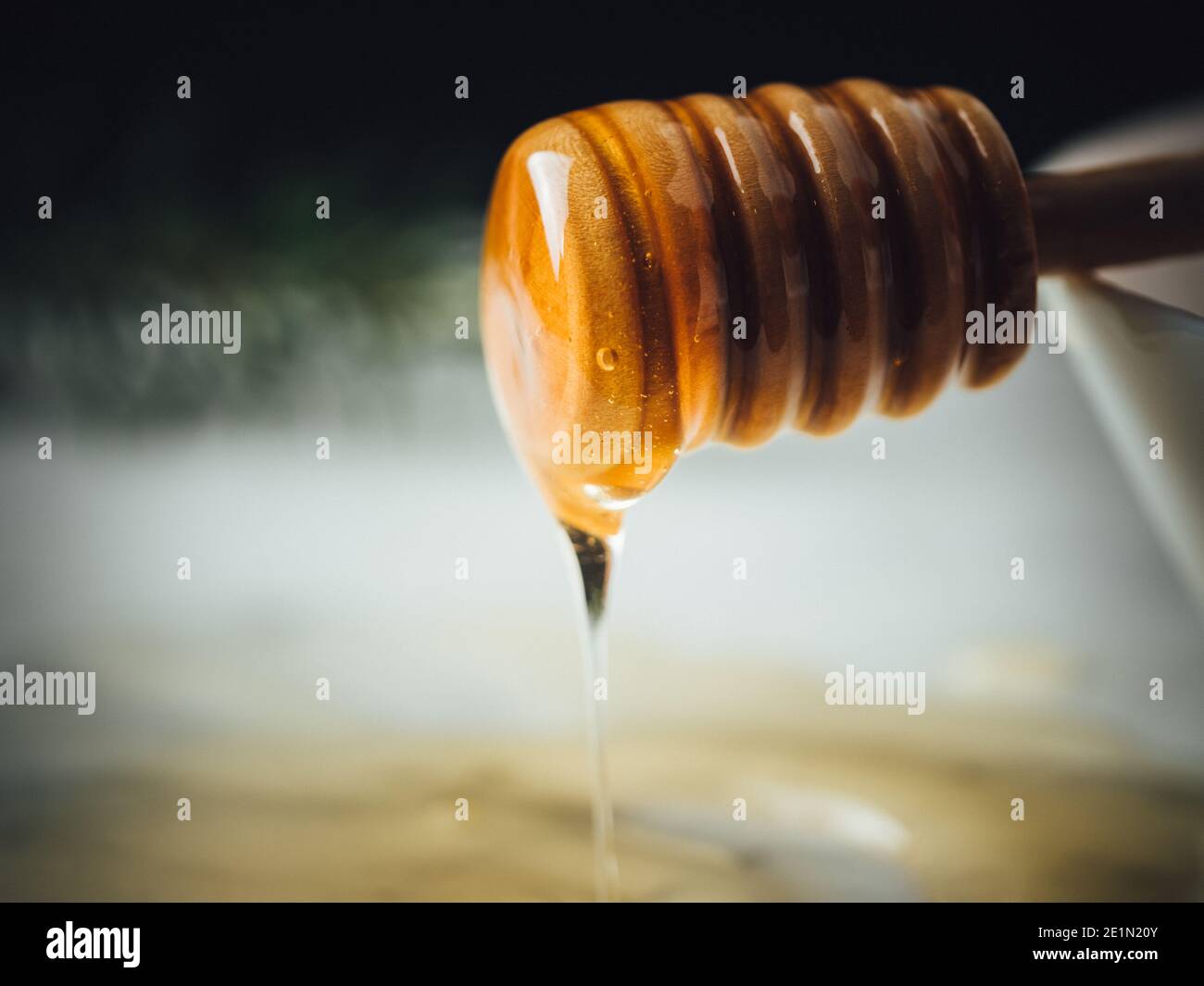 Honey wood dipper is pouring honey. Honey dripping on white marble top
