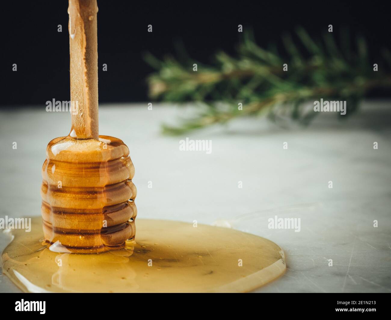 Honey wood dipper is vertical on drop of honey. Honey dripping on white