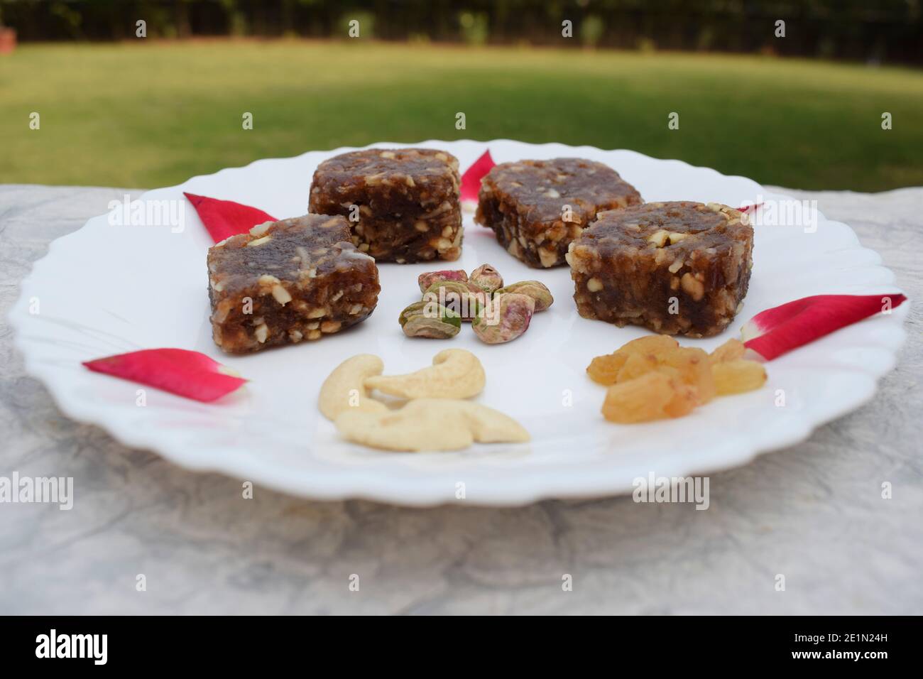 Khajur ka halwa or khajoor paak is a traditional Indian and Pakistani dish. dry fruit halwa barfi dates decorated with red pink rose petals and served Stock Photo