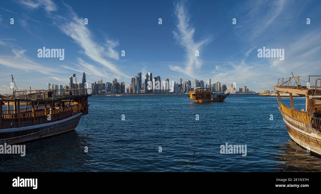 Doha skyline from the corniche promenade afternoon shot showing dhows with Qatar flag in Arabic gulf in foreground and clouds in the sky in background Stock Photo