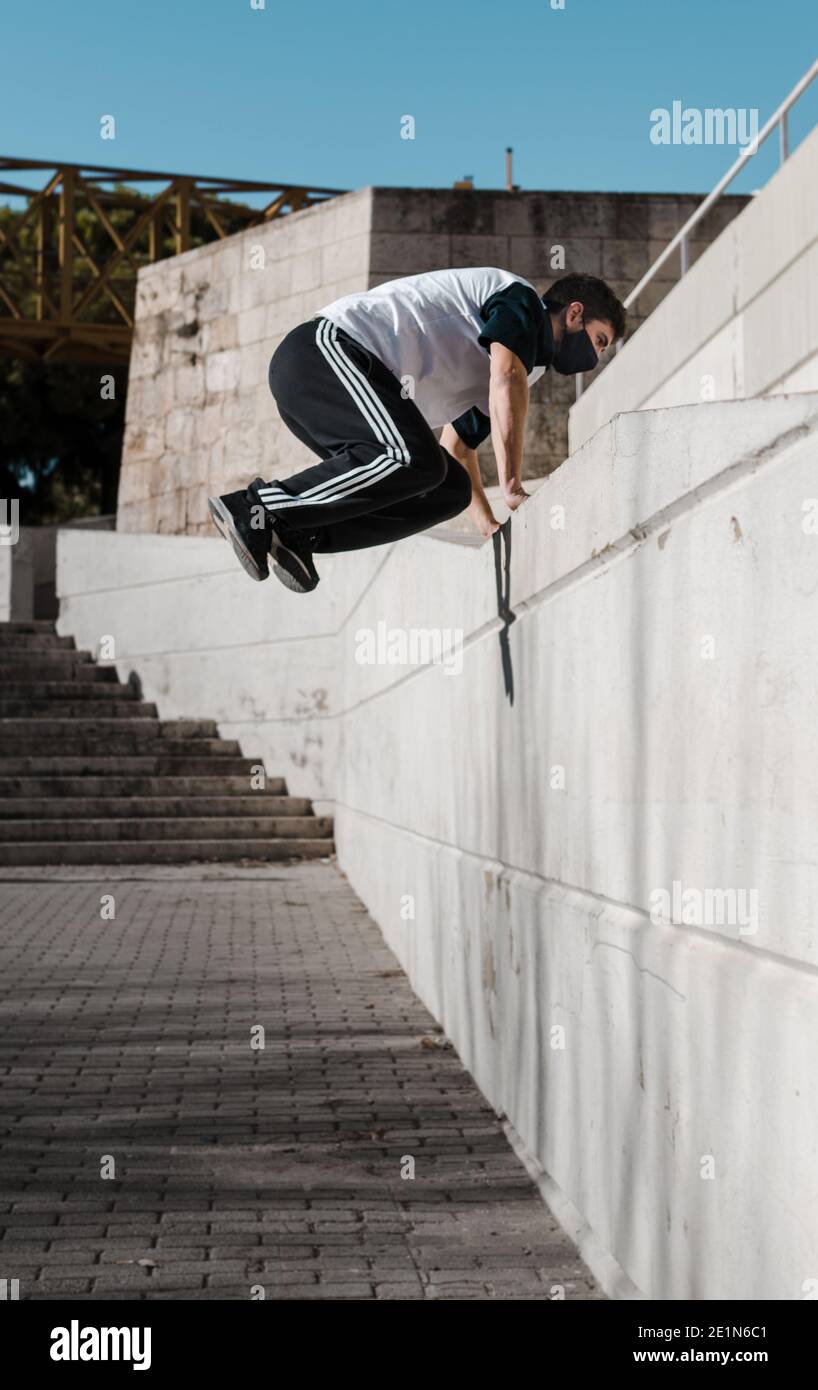 young man wearing a mask jumping a high wall. Training parkour in an urban  environment. Stairs in the background Stock Photo - Alamy