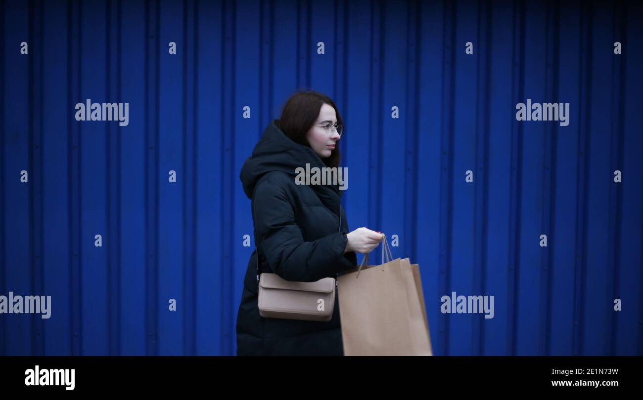 young woman in winter clothes with paper bags with purchases on blue background Stock Photo