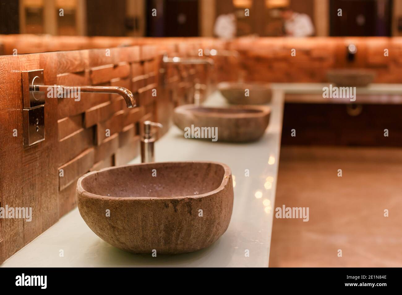 Stylish sink made of light natural stone. Bathroom with stone washbasin on a wooden top in a tropical loft style. Stock Photo