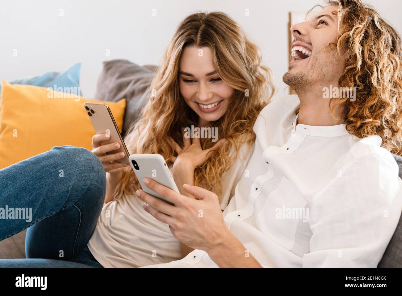 Delighted beautiful couple laughing and using cellphones while resting ...