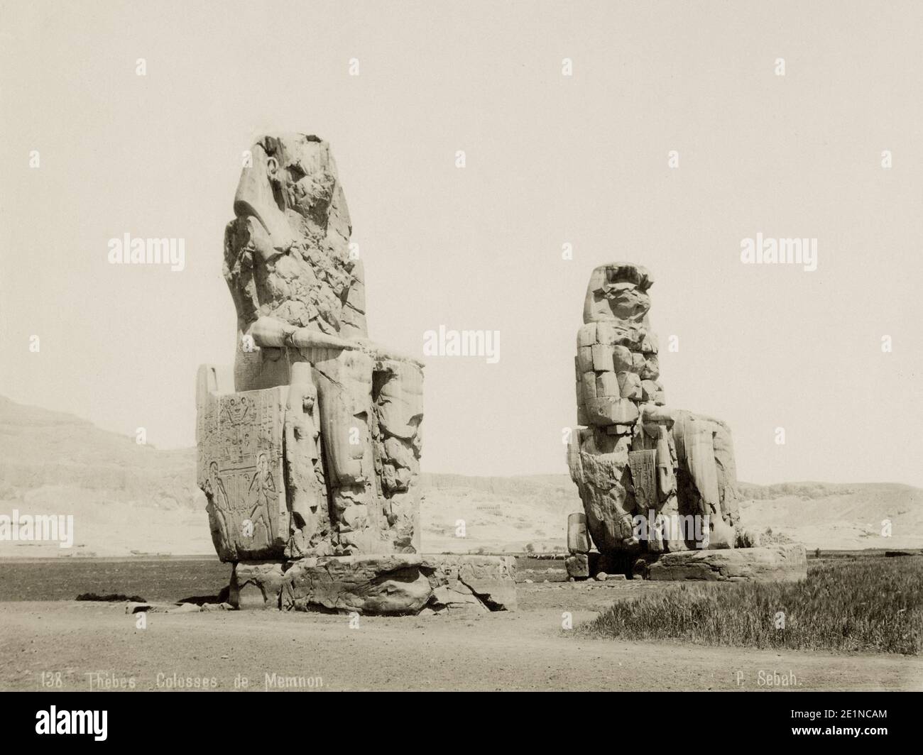 19th century vintage photograph: Thebes, Egypt, The Colossi of Memnon. The Colossi of Memnon are two massive stone statues of the Pharaoh Amenhotep III, who reigned in Egypt during the Eighteenth Dynasty of Egypt. Since 1350 BCE, they have stood in the Theban Necropolis, located west of the River Nile from the modern city of Luxor. c.1880's. Stock Photo