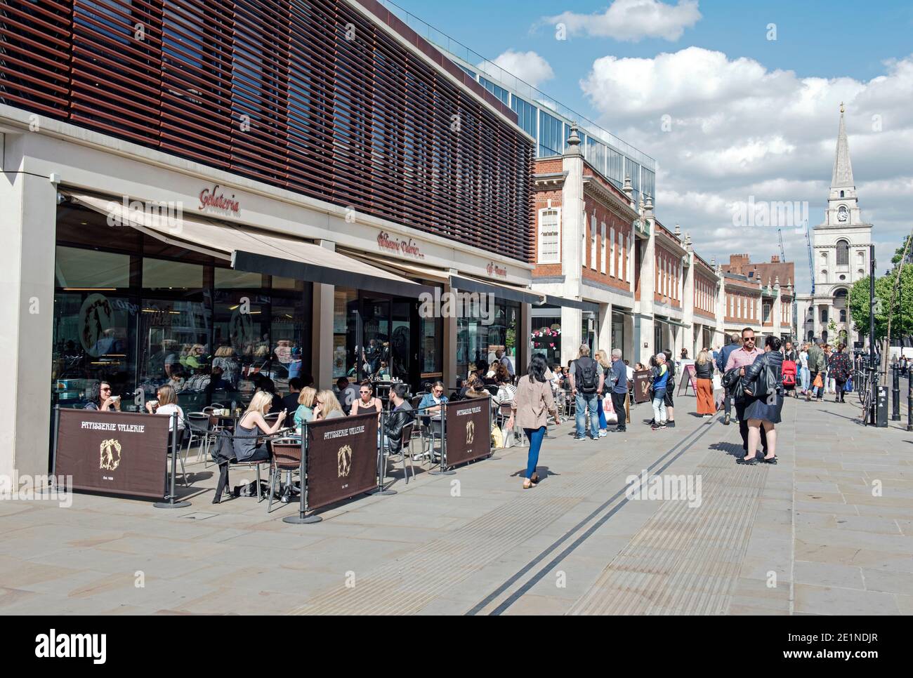 Busy street scene with people siting and eating outside Patisserie Valerie in pedestrianised Brushfield Street with Christ Church in distance Spitalfi Stock Photo
