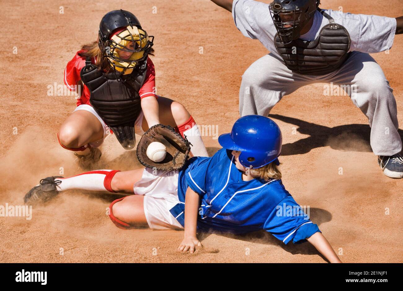Softball player sliding into home plate while umpire rules safe Stock Photo