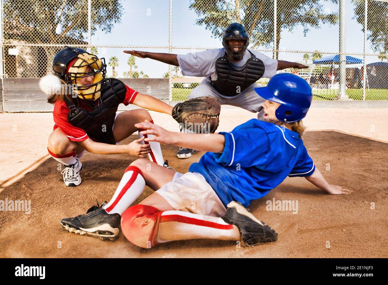 Portrait of Softball player sliding into home plate while umpire rules safe Stock Photo