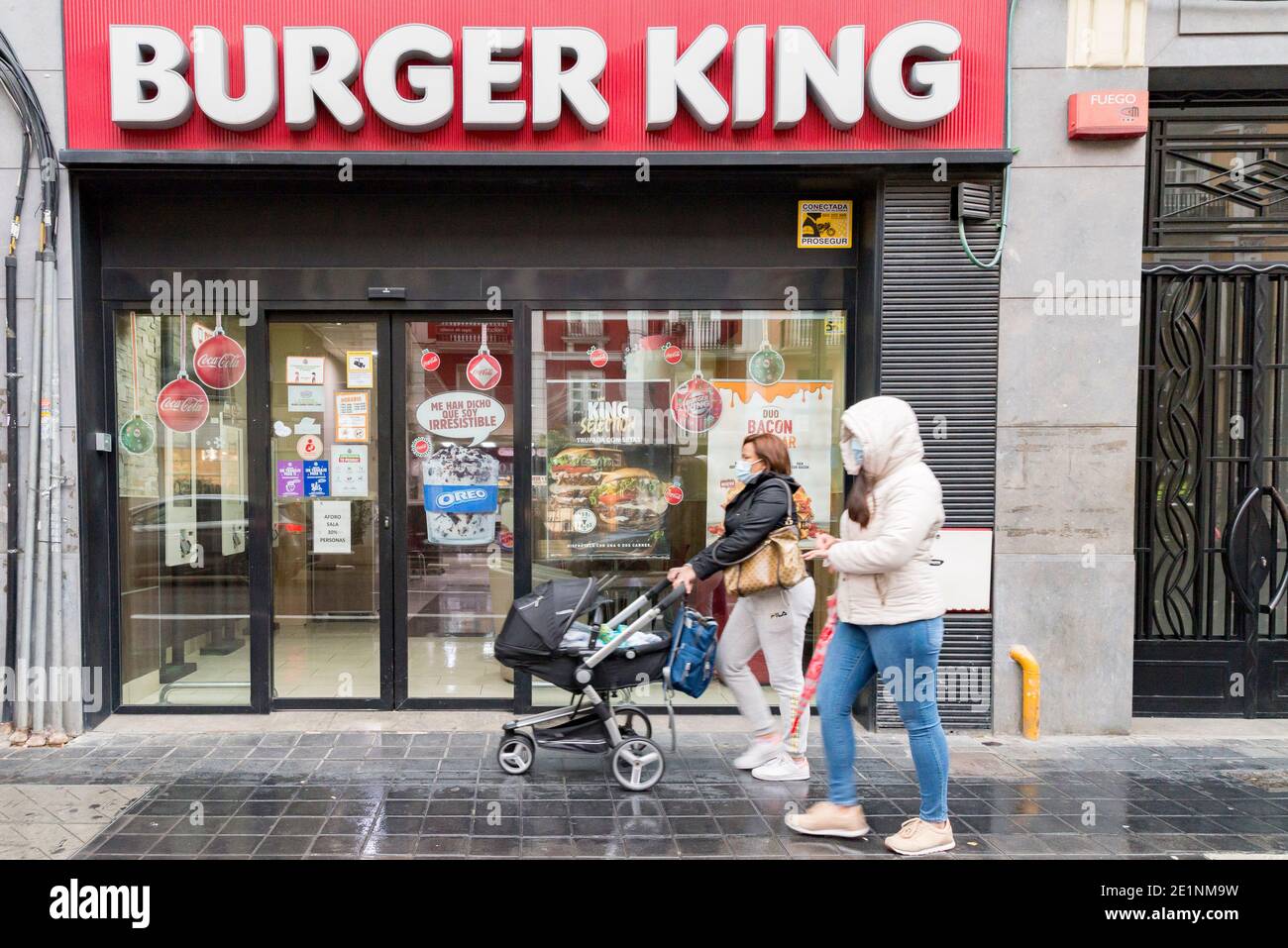 People wearing face masks walk past the Burger King fast food restaurant.In the last weeks of Christmas, the cases of Covid19 in Valencia have increased, this has caused the winter sales to begin accompanied by new anti-Covid measures that also affect the hostelry sector. Until January 31, bars and restaurants will close at 5pm and maximum of four people per table. The capacity is reduced to 30% in shops and night mobility until 10 pm. Stock Photo