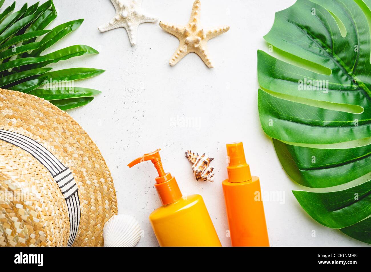 Sunscreen bottles arranged with straw hat on white background with palm leaves, top view Stock Photo