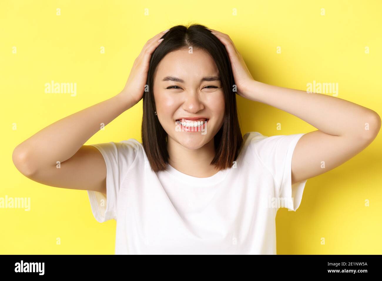 Close up of happy asian girl touching her hair and smiling, standing in ...