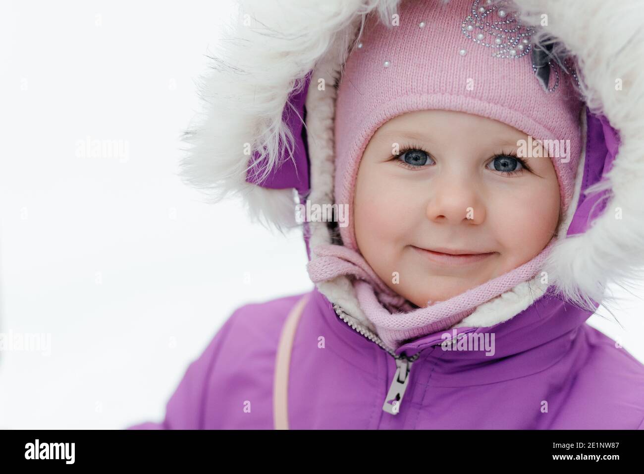 Portrait of a little smiling girl in a pink cap on the street against a background of snow Stock Photo