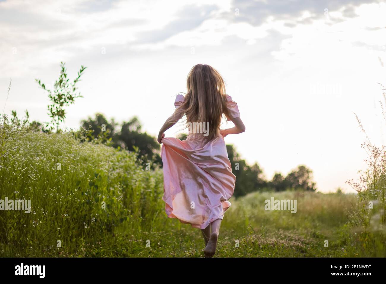 girl running across the field in a pink dress Stock Photo