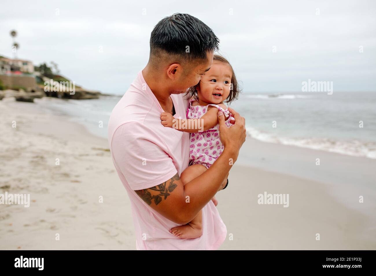 Adoring Asian dad with crewcut holds sweet smiling daughter at beach Stock Photo
