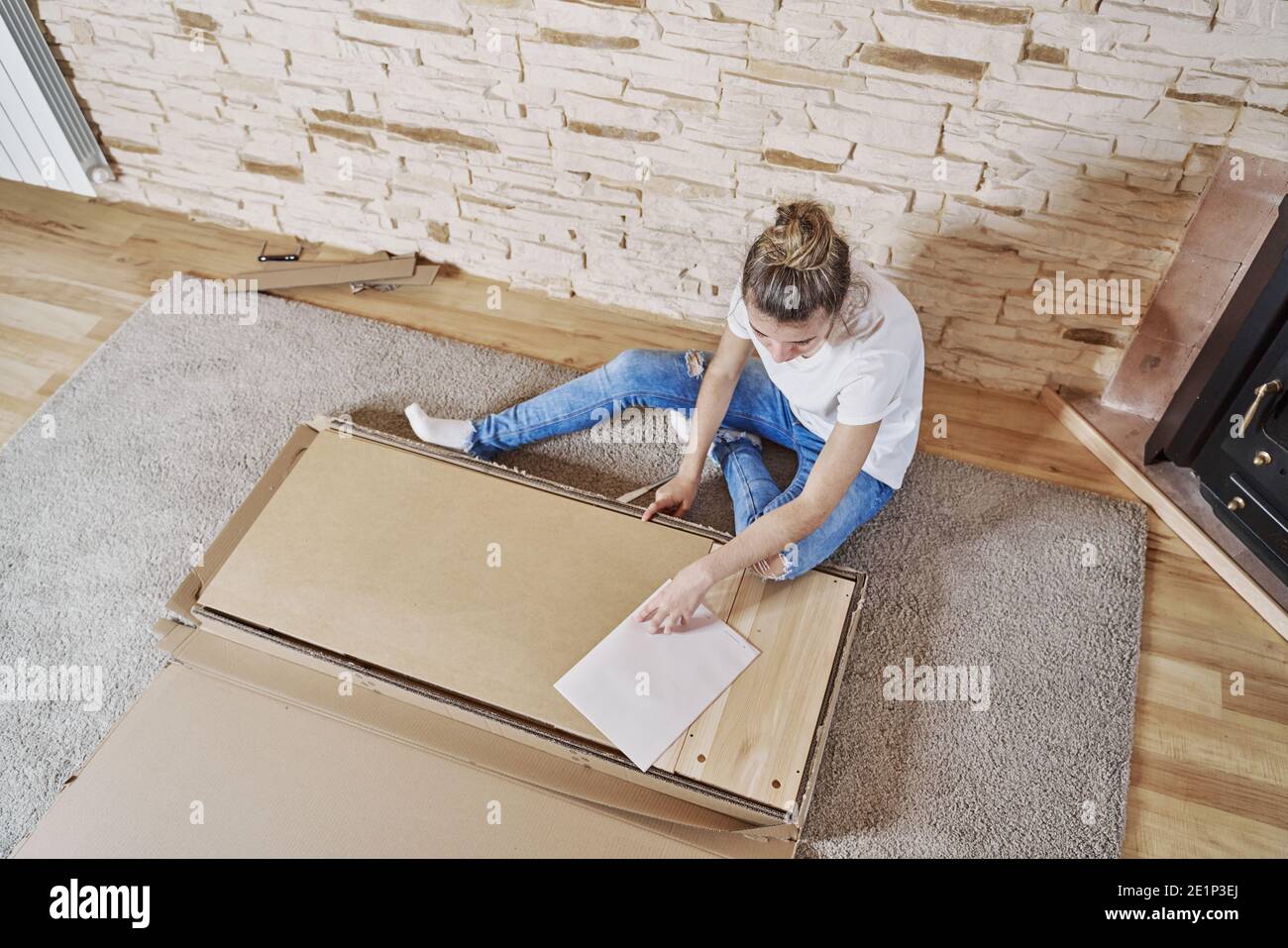 Above view of girl opening a paperboard box with a knife. The box is on the floor and the woman sitting. Horizontal photo Stock Photo