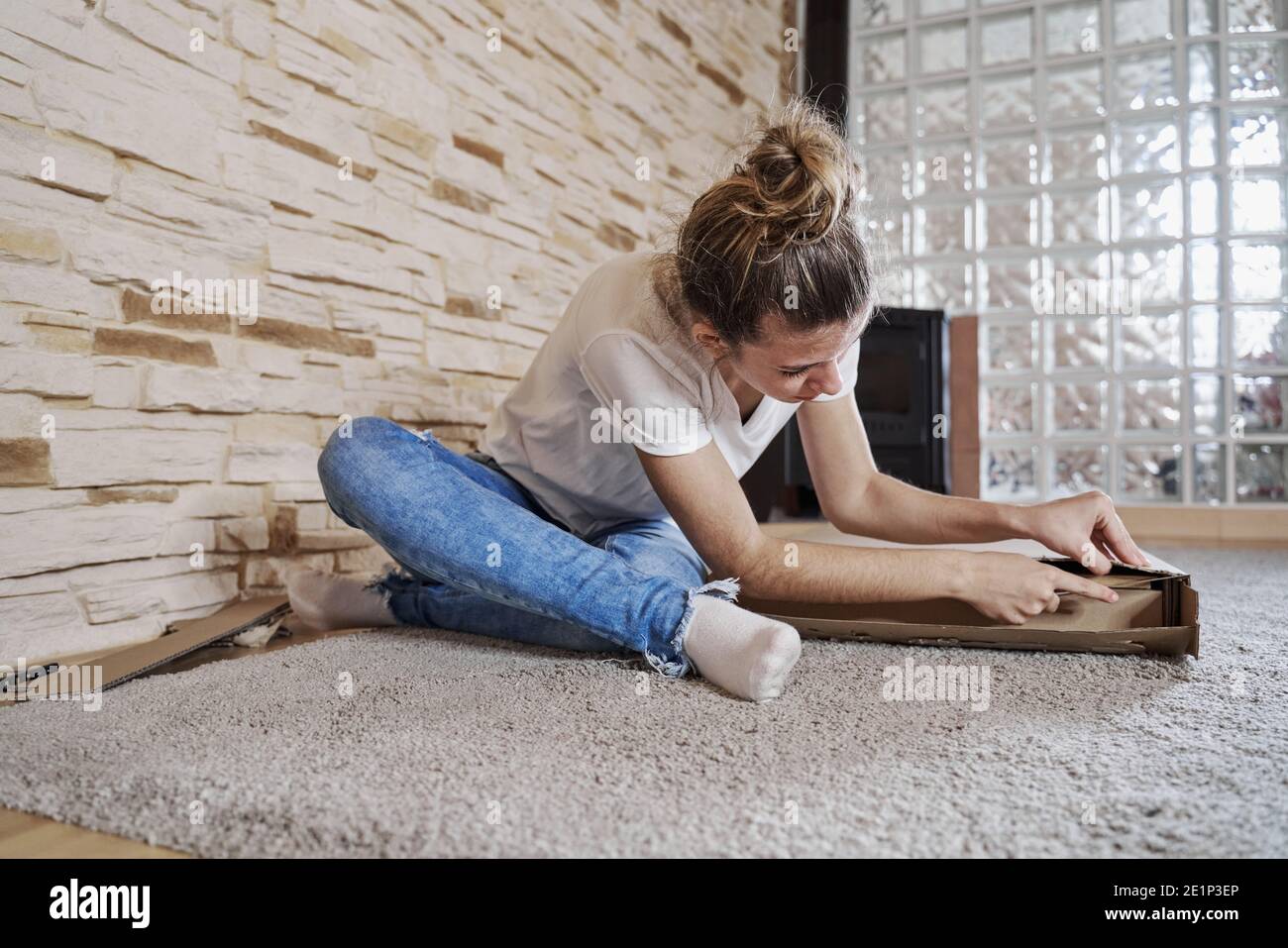 front view of girl opening a paperboard box with a knife. The box is on the floor and the woman sitting. Horizontal photo Stock Photo