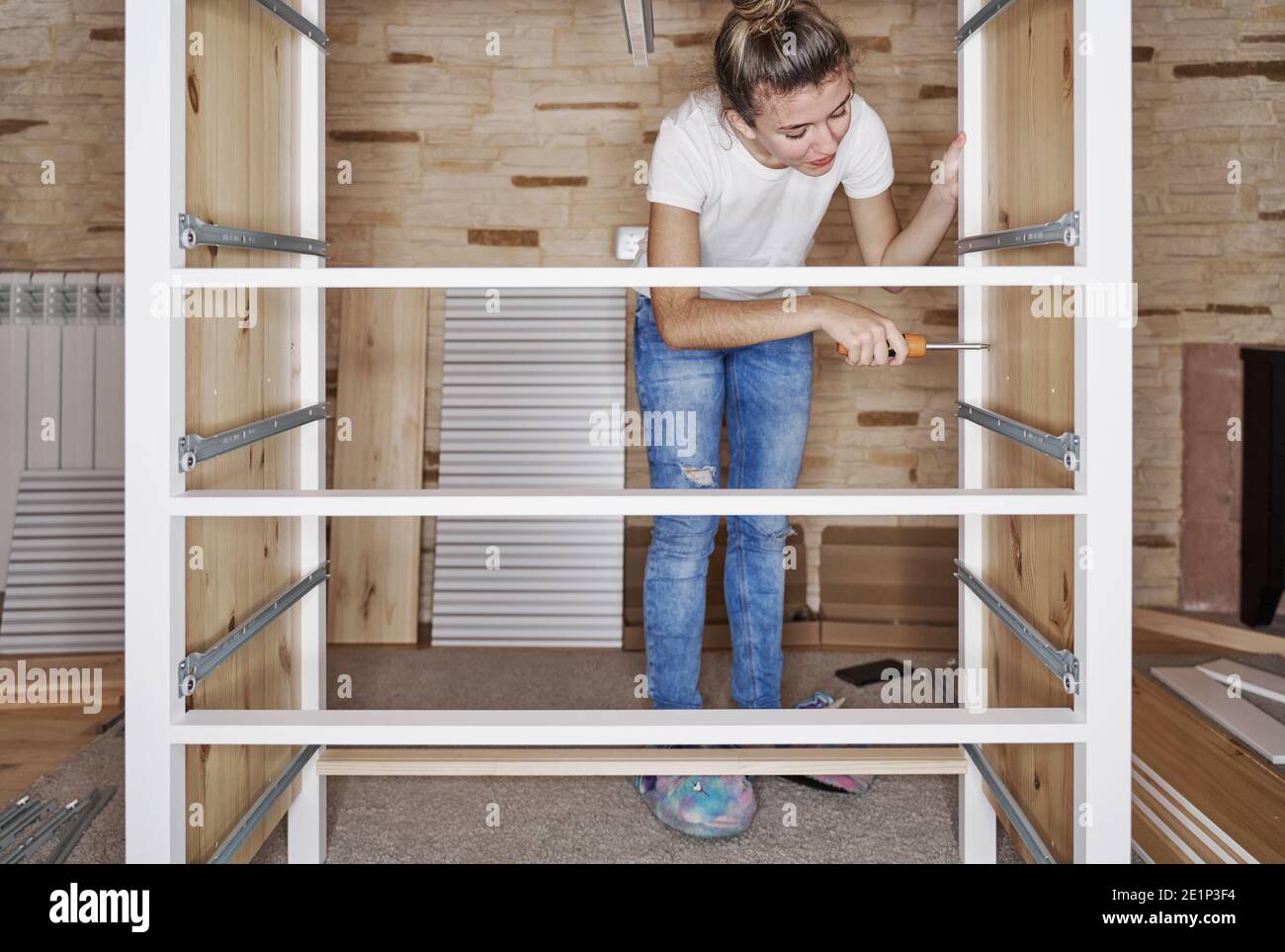 Front view of a young blonde girl screwing a screw with a screwdriver in a  strip of a furniture assembling by herself a wardrobe of wood. Horizontal p  Stock Photo - Alamy