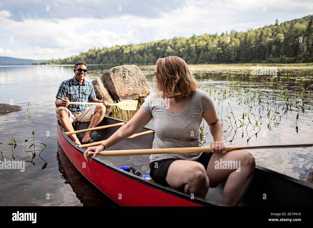 African man and white woman in red canoe on lake in Maine woods. Stock Photo