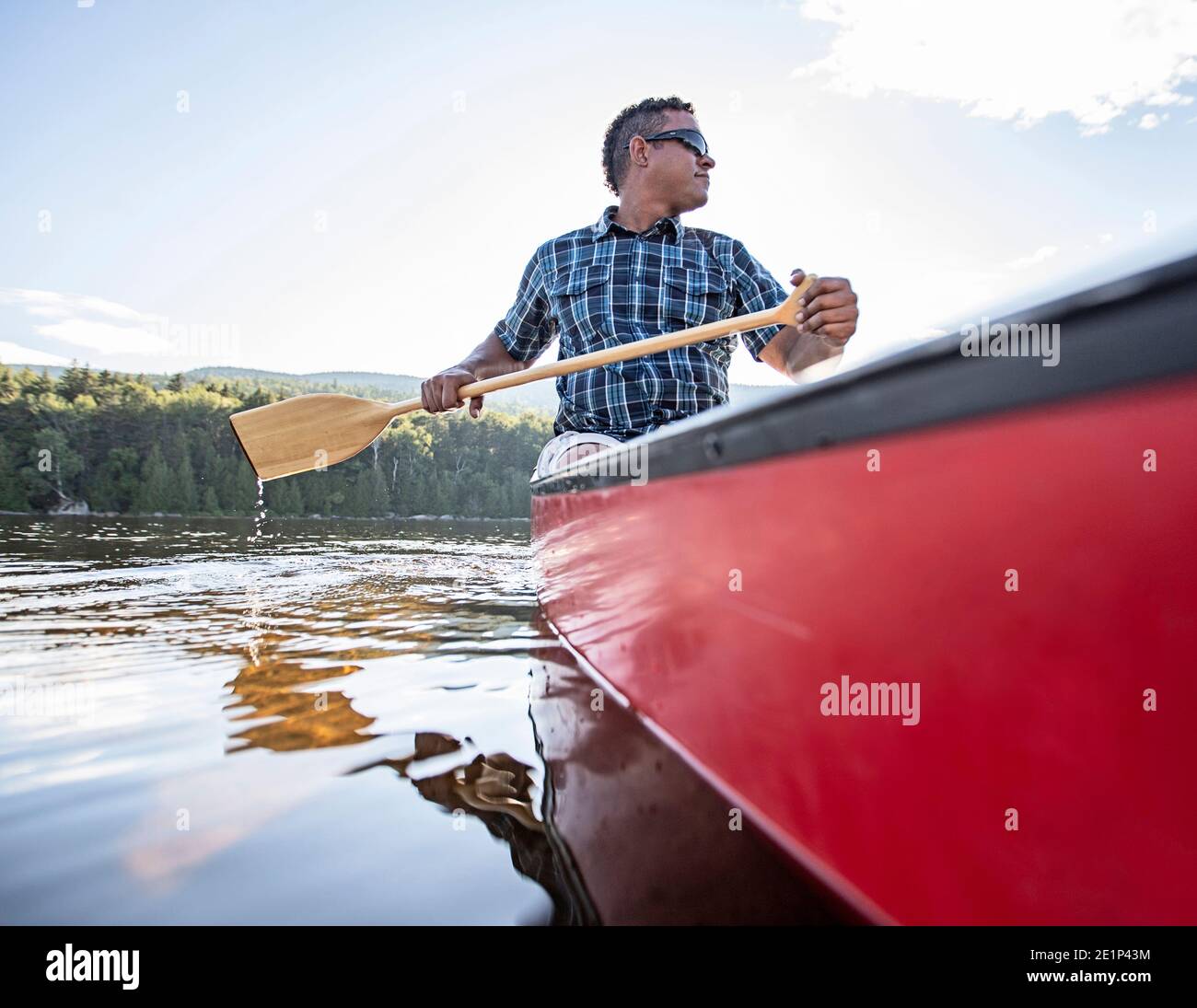 African American male paddles red canoe on peaceful lake in Maine Stock Photo