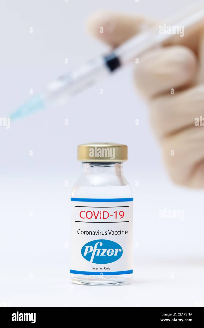 Bottle of coronavirus vaccine with the Pfizer logo and dr hands with syringe background. Stock Photo