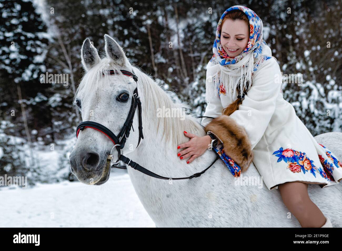 Pretty woman in traditional clothes is riding her horse (focus on the horse's face) Stock Photo