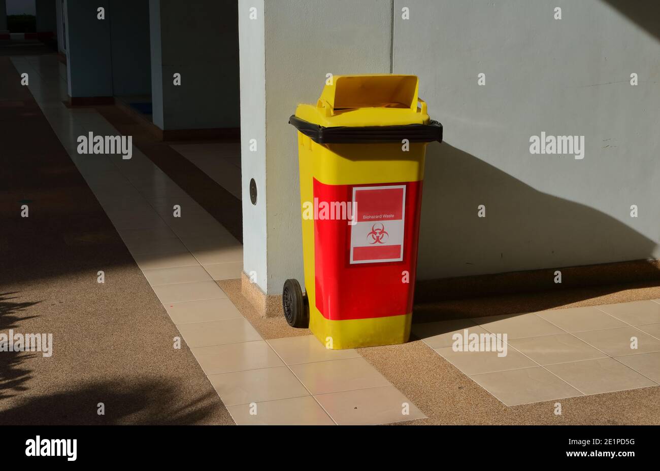 Biohazard waste bin standing on tiled floor against blue wall under sunlight Stock Photo