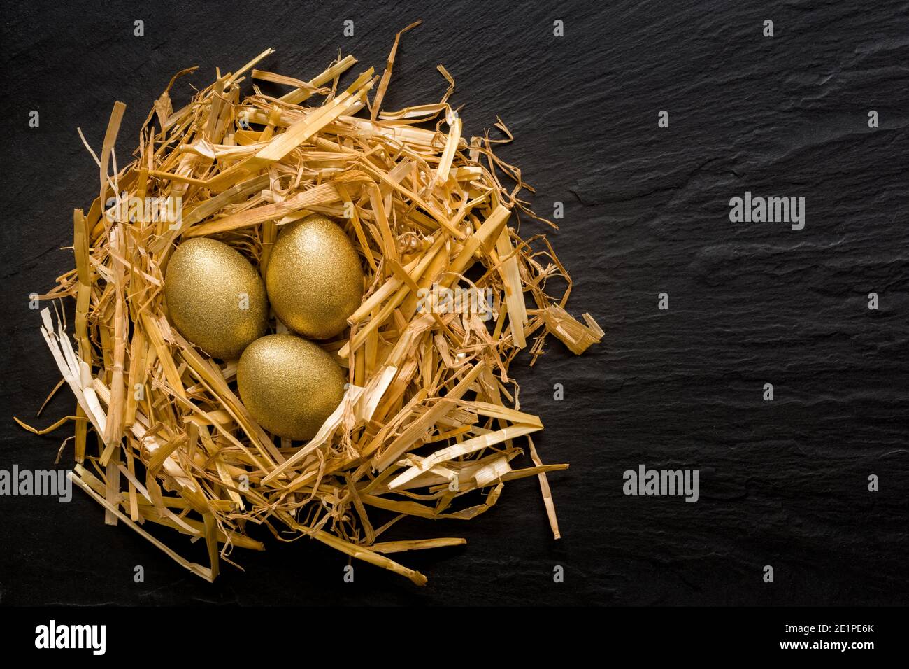 Three golden eggs in the grassy nest on black slate background with copyspace Stock Photo