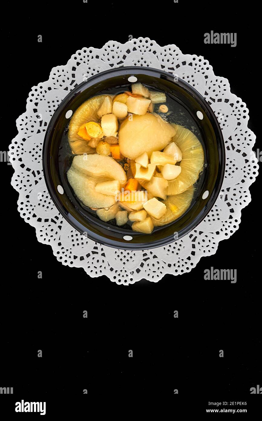 Fruit cocktail in a black bowl with white spots on a white doily. Stock Photo