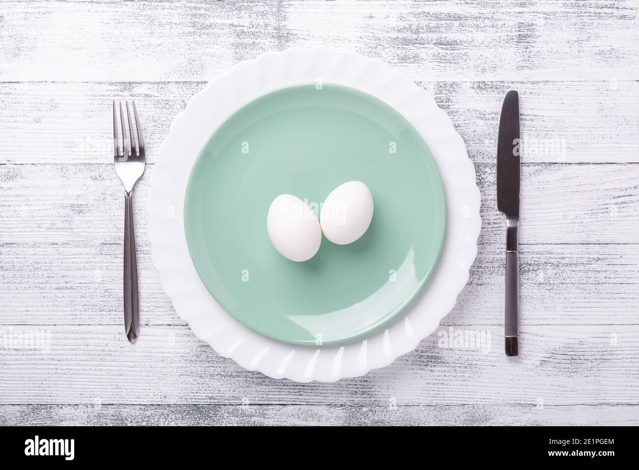 Spring table setting. Green mint plate, Easter eggs and cutlery on wooden background. Easter composition. Copy space. Top view - Image Stock Photo