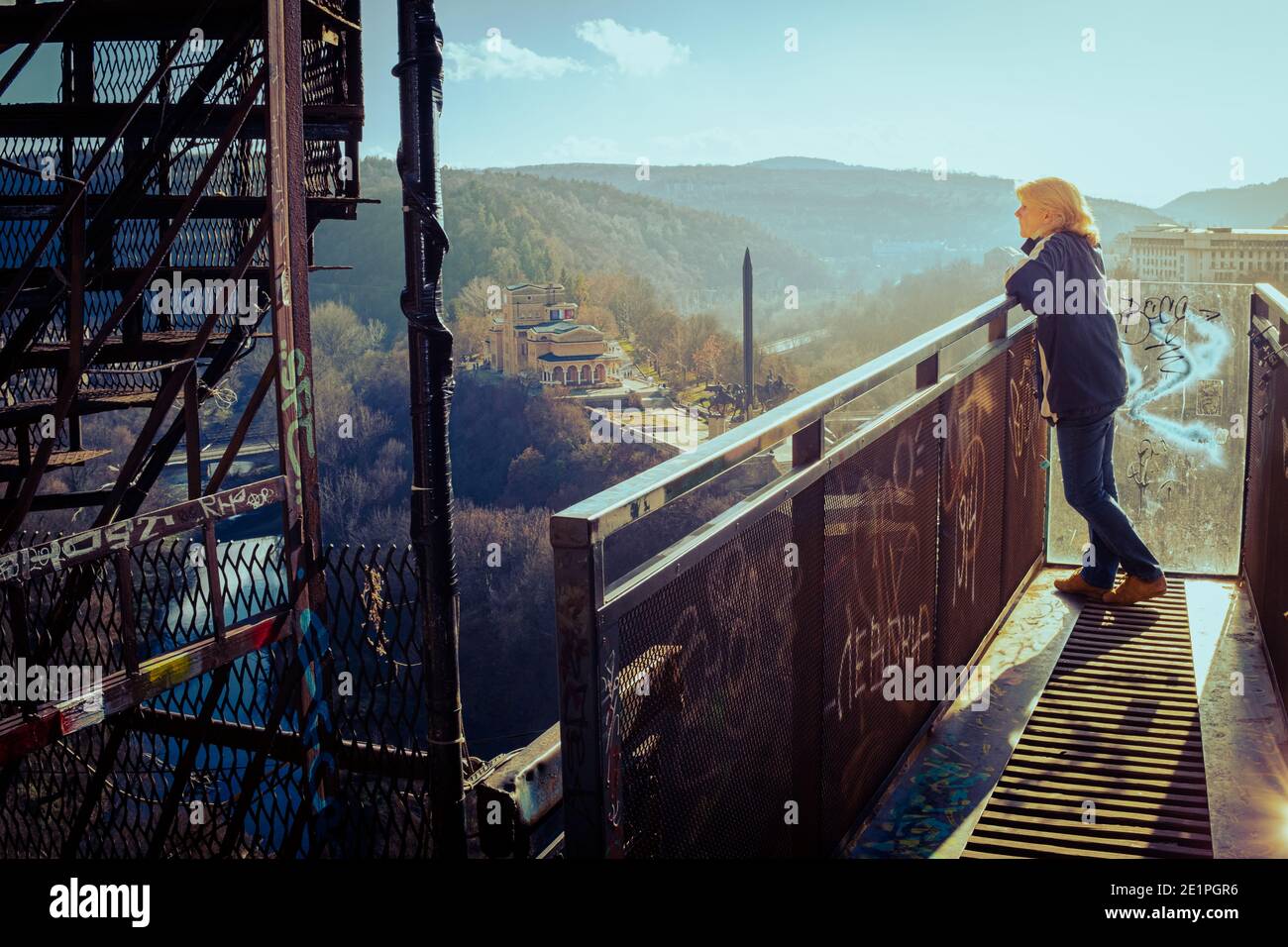 Woman on elevated walkway platform overlooking Assens monument and river Yantra in city of Veliko Tarnovo on new years winter day. Stock Photo