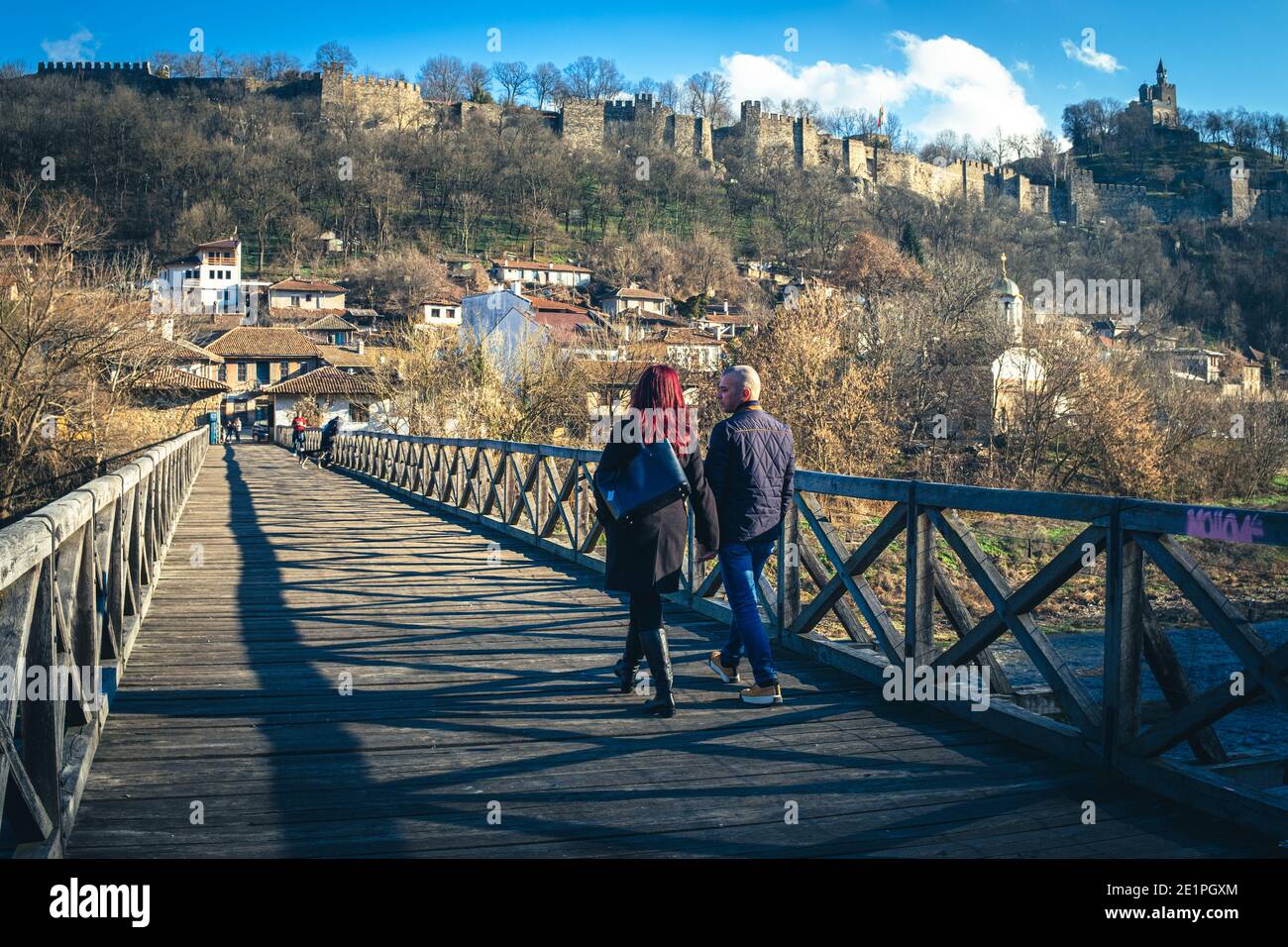 Couple walking on bright new years day over Bishops bridge in old quarter of Veliko Tarnovo with Tsarevets medieval castle in background. Stock Photo