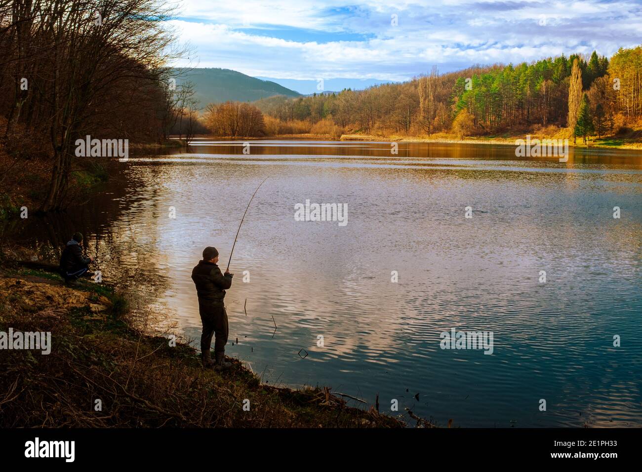 Silhouette of fisherman in the shade reeling in his line on the banks of the reservoir, Sinkevitsa, on a sunny day in winter Stock Photo