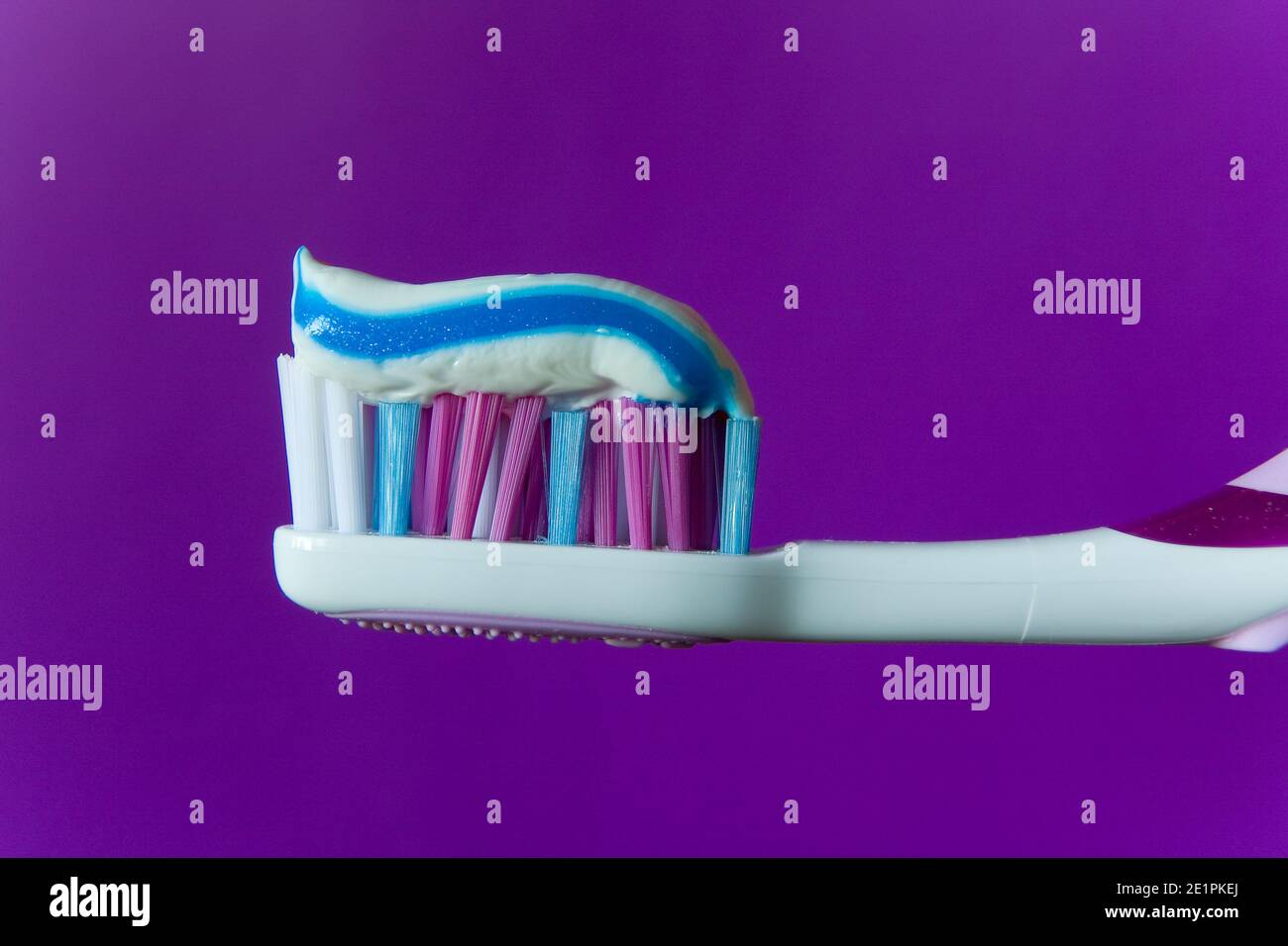A multi-colored toothpaste is applied to a multi-colored toothbrush. Macro. Stock Photo