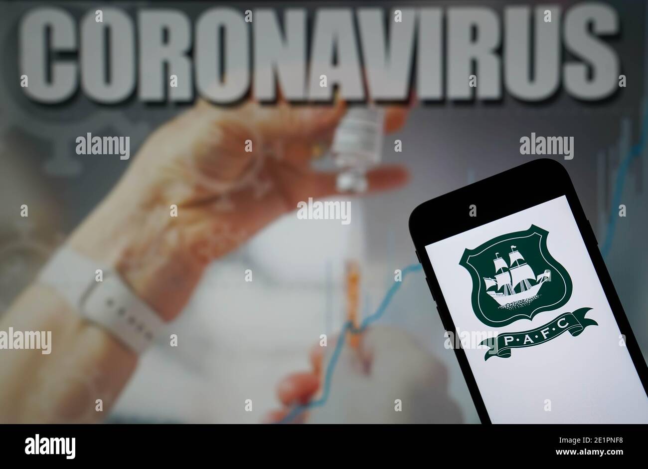 The Plymouth Argyle Football Club logo seen displayed on a mobile phone with a Coronavirus illustration on a monitor in the background Stock Photo