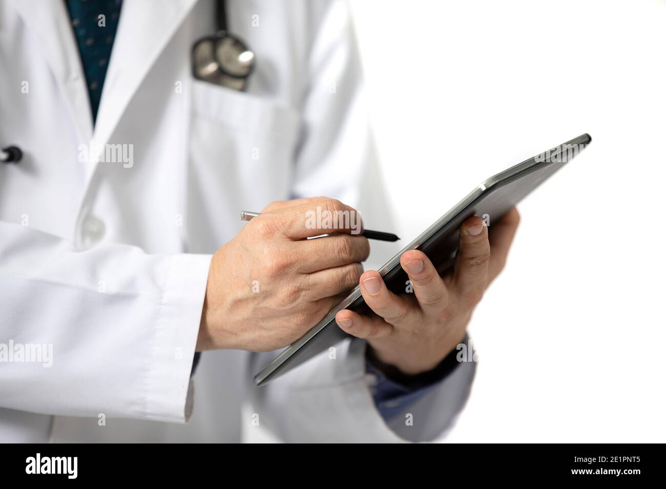 A standing male doctor in long white hospital gown writing on a tablet. Isolated on white background. Stock Photo