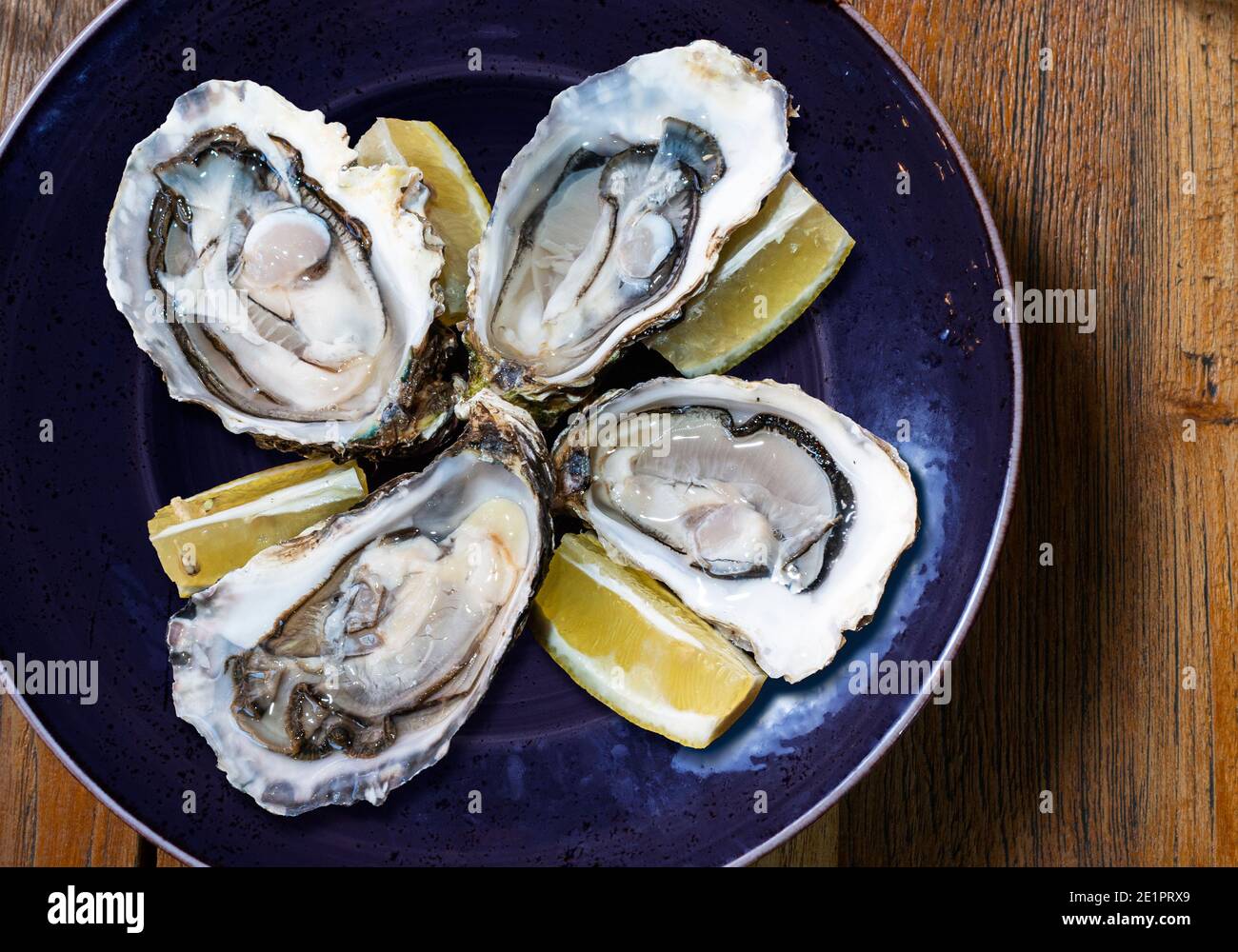 Blue plate with four open oysters and lemon Stock Photo