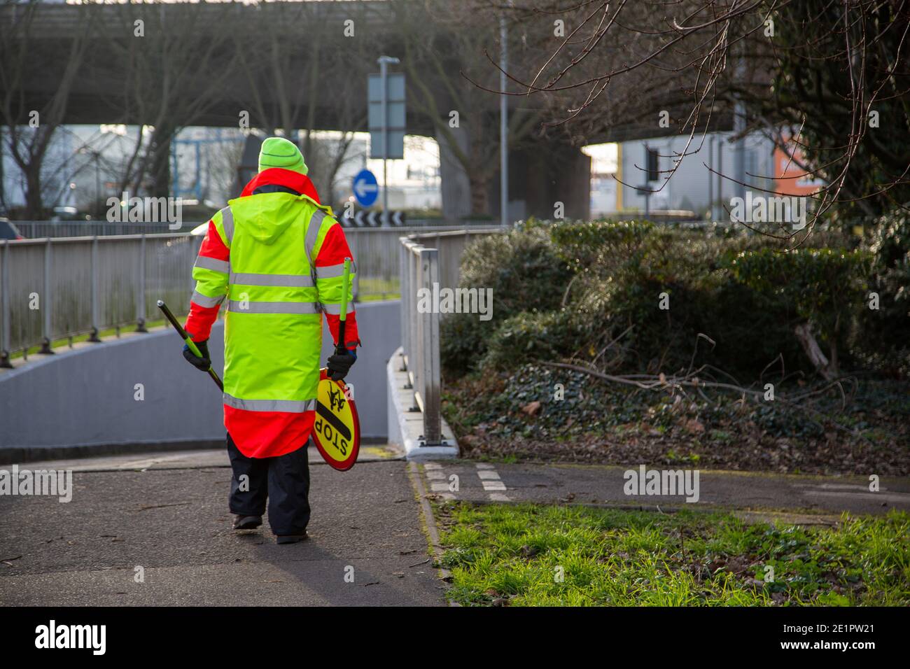 A lollypop man walking to work wearing high visibility clothing and carrying his lollypop stick that is used for school crossing Stock Photo