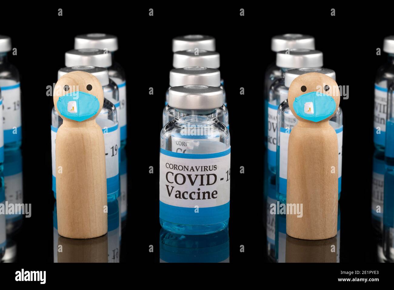 Wooden models wearing blue face masks with glass vials labelling Covid-19 vaccine. Stock Photo